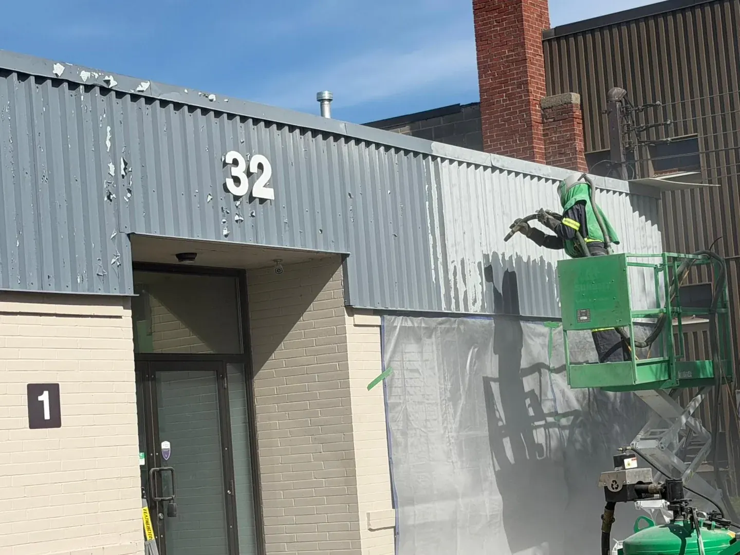 Pure Blast Solutions technician on a lift dustless sandblasting paint off the metal cladding of a commercial building in the GTA